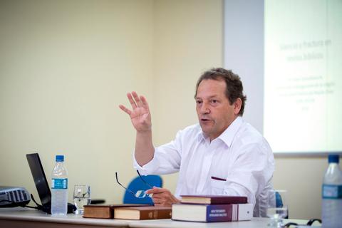 Un hombre está dando una charla en una sala, gesticulando mientras habla.
