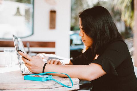 Una mujer utiliza una computadora portátil mientras sostiene un teléfono móvil en un entorno acogedor.