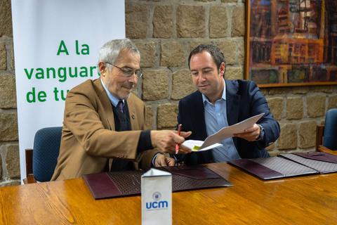 Dos hombres firmando un documento en una mesa de trabajo.