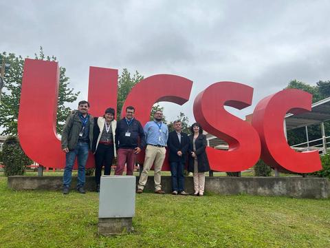 Un grupo de personas posando frente a un gran cartel con las siglas UCSC en un entorno al aire libre.