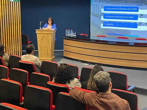 Una mujer presenta en una sala de conferencias frente a un público sentado.