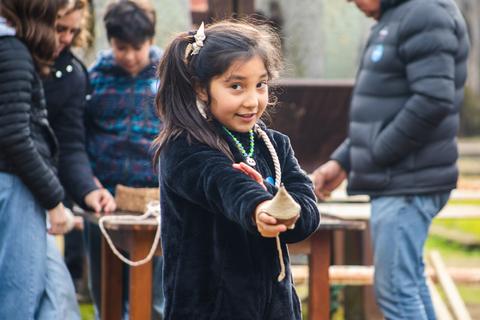 Una niña sonriente muestra un objeto de arcilla mientras disfruta de un día al aire libre con otros niños.