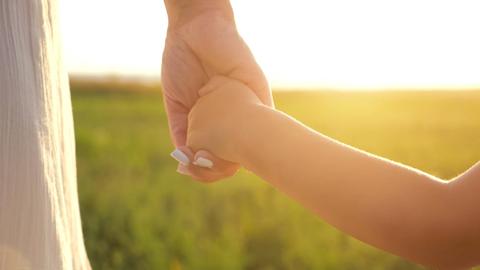Una mamá y su hijo se agarran de la mano al atardecer en un campo verde.