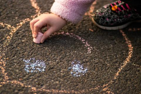 Una niñita dibujando con tiza en el suelo.