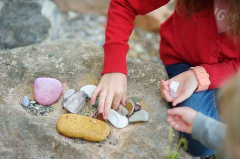 Dos niñ@s jugando con piedras de colores en una roca.