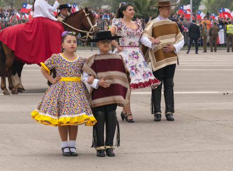 En la imagen se aprecia a niños y adultos vestidos con trajes tradicionales chilenos, celebrando una festividad patria.