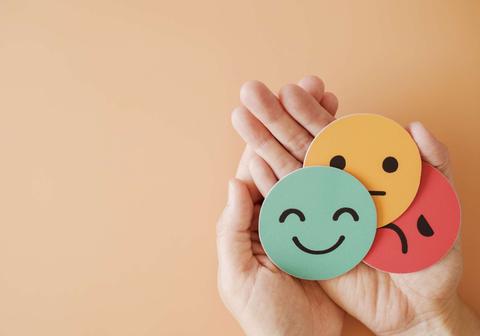 Una mano sostiene tres círculos de colores con caras felices y tristes.
