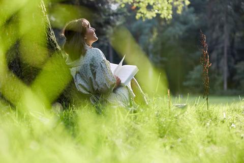 Una mujer relajándose en un bosque mientras lee un libro.