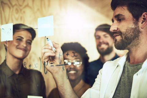 Un grupo de personas observa a un hombre mientras escribe en una pizarra de vidrio.