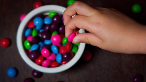 Una mano tomando un caramelo de colores de un tazón.