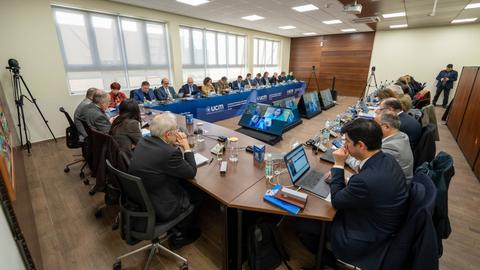 Una reunión formal con varios participantes discutiendo en una sala moderna.