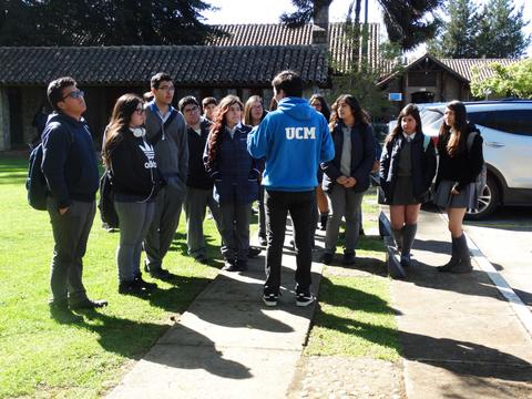 Un grupo de estudiantes escucha atentamente a un orador en un entorno al aire libre.