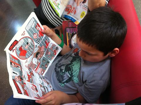 Un niño lee un cómic mientras está sentado en un sofá rojo.