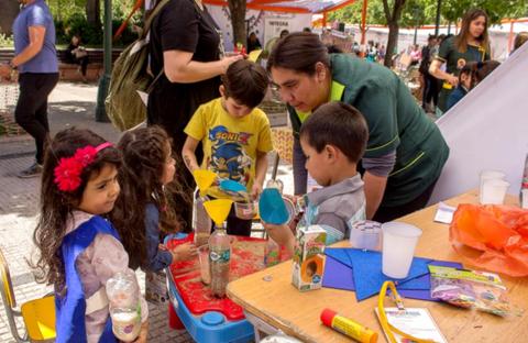 Un grupo de niños y un adulto participan en una actividad educativa al aire libre, manipulando materiales en una mesa.