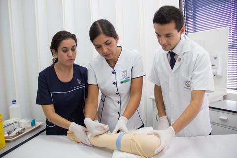 Tres personas trabajando en una práctica de atención médica con un maniquí en un entorno clínico.