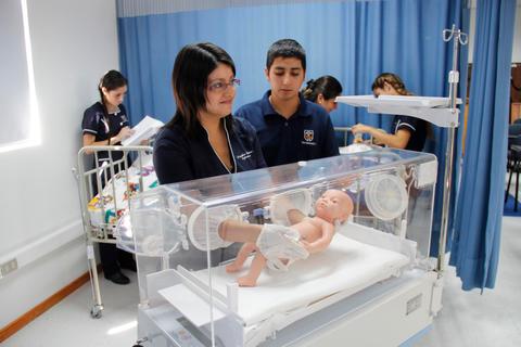 Una madre cuida a su bebé en una incubadora mientras otros profesionales de la salud están en el fondo.