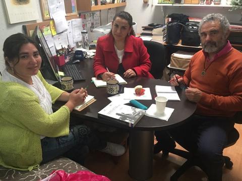 Un grupo de tres personas conversando en una oficina mientras están sentados alrededor de una mesa.