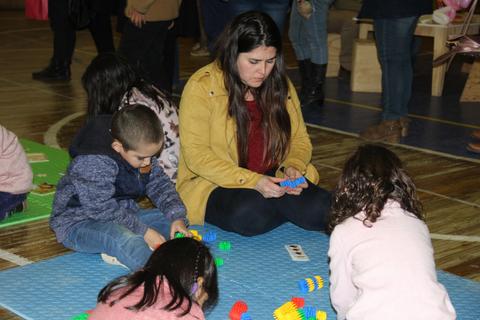 Un grupo de niños y una adulta juegan con juguetes de construcción en un ambiente alegre.
