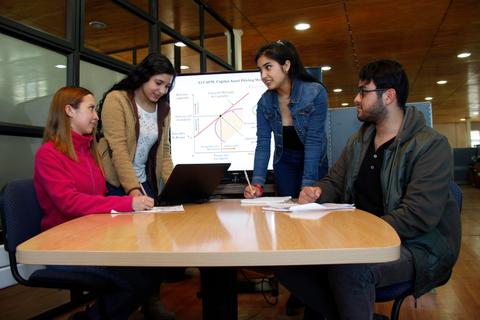 Un grupo de cuatro estudiantes colaborando en un proyecto frente a una computadora en un ambiente de trabajo.