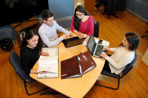 Cuatro personas se encuentran alrededor de una mesa trabajando y colaborando en un proyecto.