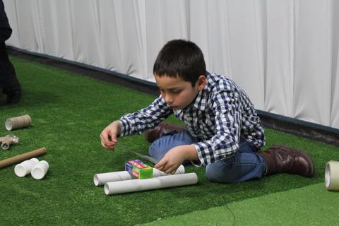 Un niño está sentado en el suelo jugando con tubos de cartón y una caja de colores.