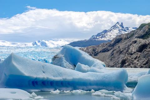 Un paisaje glacial con icebergs y montañas en el fondo bajo un cielo azul.