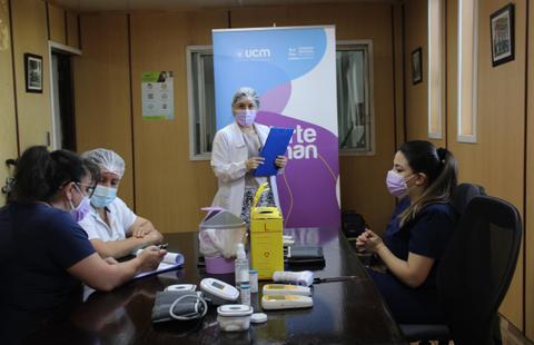 Un grupo de profesionales de la salud se reúnen en una oficina, donde una persona está presentando información mientras los demás observan.