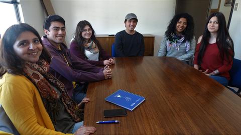 Un grupo de seis personas se sientan alrededor de una mesa de madera en un entorno interior.