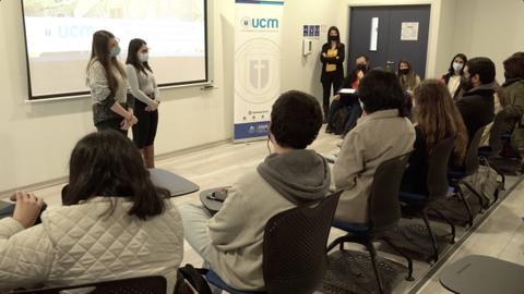 Un grupo de personas asiste a una presentación en una sala con pantallas y una mesa.