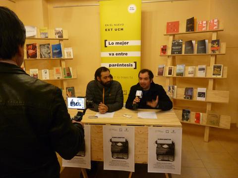 Dos hombres participan en una charla en un evento literario rodeados de libros.