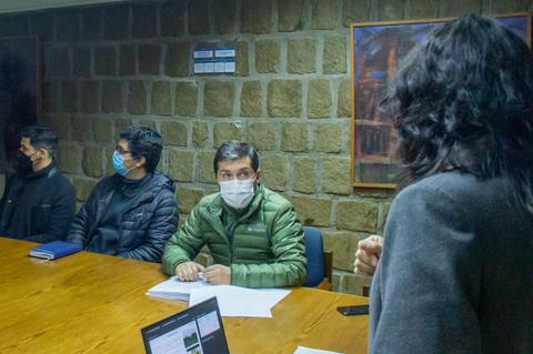Un grupo de personas se encuentra en una reunión sentados alrededor de una mesa, con algunos usando mascarillas.