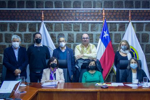 Reunión de un grupo de personas en un entorno formal con banderas chilenas en el fondo.