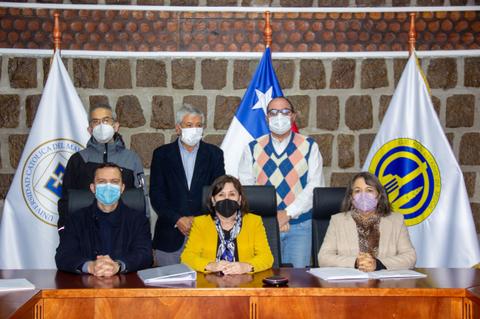 Un grupo de personas en una ceremonia oficial con banderas de Chile y de una universidad detrás.