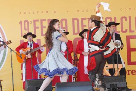 Una pareja baila en un escenario durante una fiesta tradicional con música y vestimenta típica.