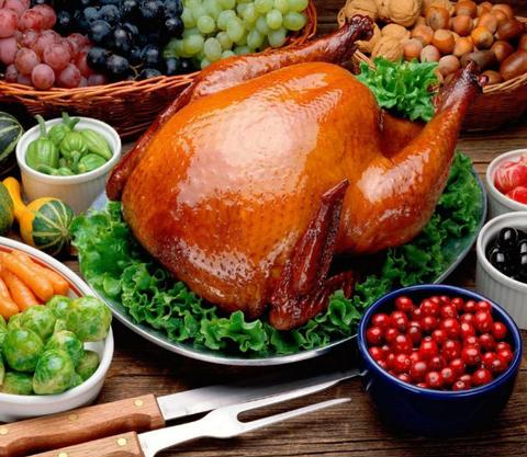 Un pavo asado sobre una cama de lechuga rodeado de diversas verduras y frutas.