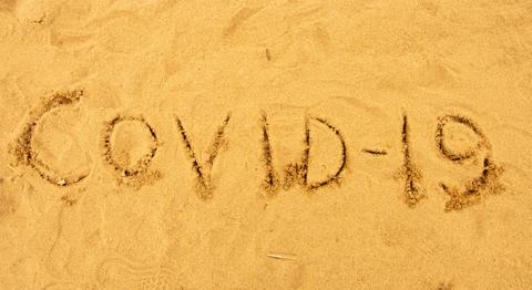 La imagen muestra la palabra 'COVID-19' escrita en la arena.