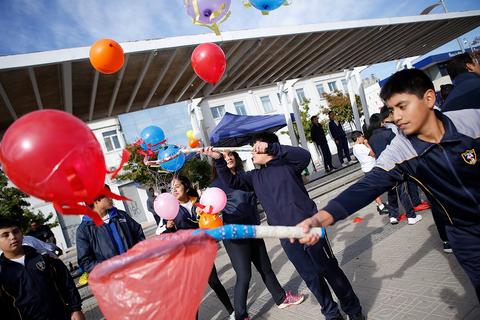 Un grupo de niños juega al aire libre en un evento escolar, lanzando globos de colores.