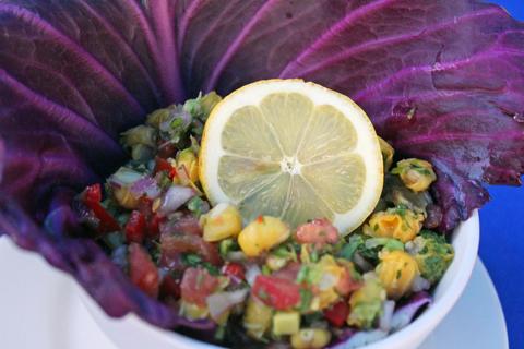 Ensalada colorida servida en una hoja de col morada con una rodaja de limón en la parte superior.
