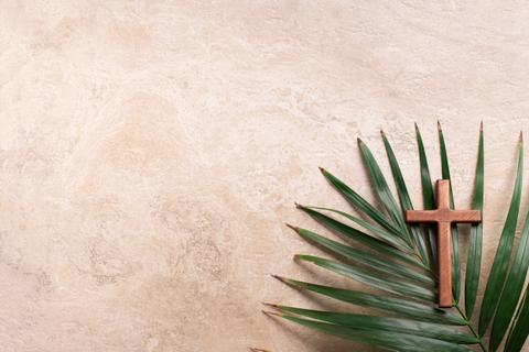Una cruz de madera sobre una hoja de palma situada en un fondo claro.