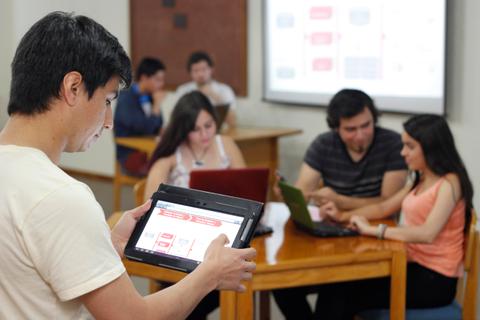 Un grupo de estudiantes trabaja en equipo en un aula utilizando dispositivos electrónicos.
