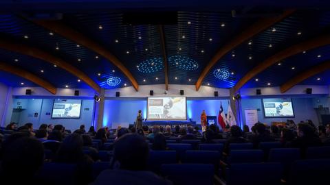 Una presentación en un auditorio con luces azules y un público atento.