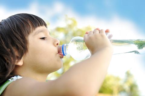 Un niño tomando agua de una botella bajo un cielo azul.