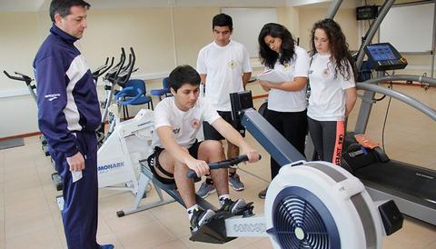 Un grupo de jóvenes está entrenando en un gimnasio, mientras un entrenador los observa.