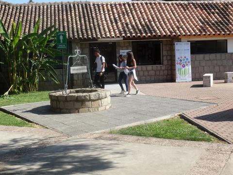 Un grupo de tres personas camina por un espacio exterior cerca de un pozo y edificios con techos de tejas.