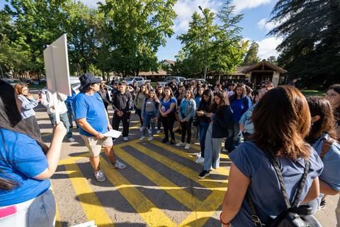 Un grupo de personas escucha atentamente a un orador en un entorno al aire libre.