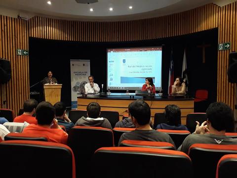 Una presentación en un auditorio con varios asistentes y un panel de ponentes en el escenario.