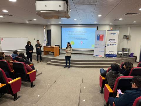 Un grupo de personas asiste a una presentación en un auditorio con pantallas y un proyector.