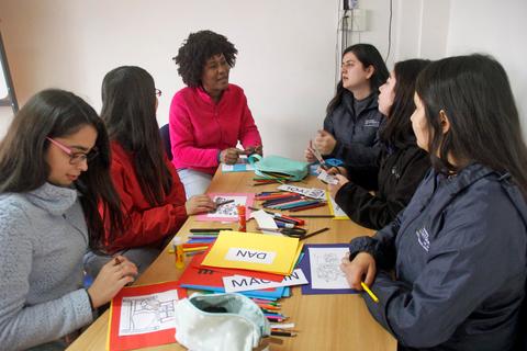 Un grupo de seis mujeres se encuentra reunido en una mesa, trabajando con materiales de arte y pinturas en un ambiente colaborativo.