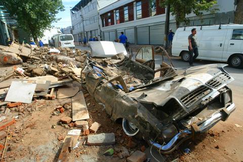 Una calle afectada por un desastre, con escombros y un coche dañado.