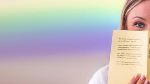 Una persona sostiene un libro frente a su cara, mostrando solo una parte de su rostro.